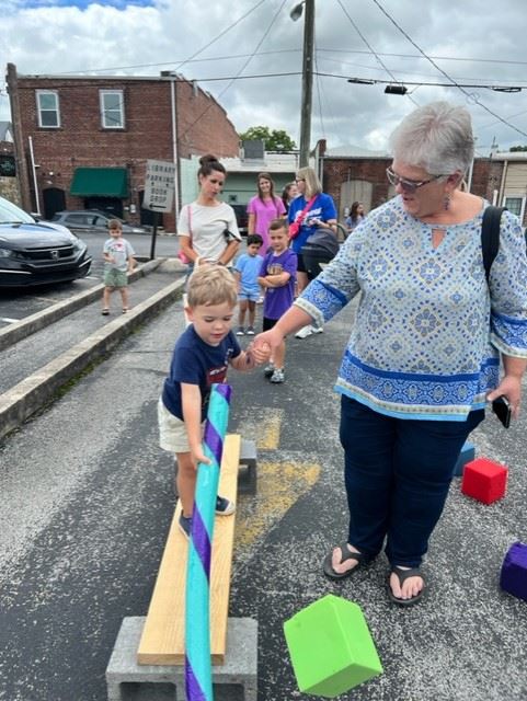 A little boy balancing on a board and swatting at a cube. 